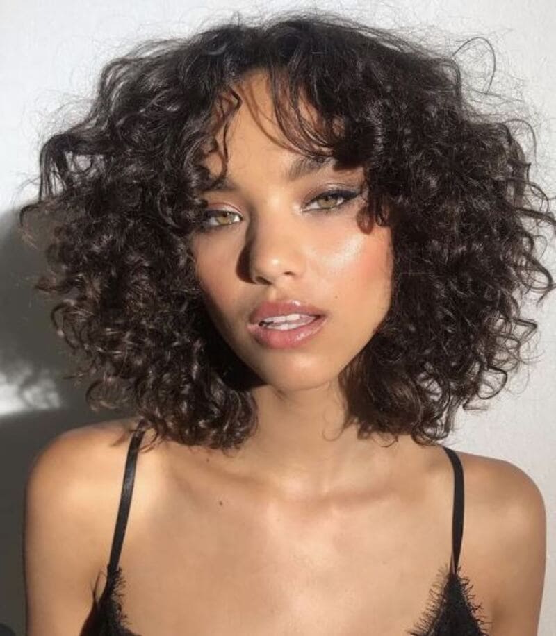 The short curly bob with curtain bangs showcases a stylish and tapered look. (Source: Pinterest)